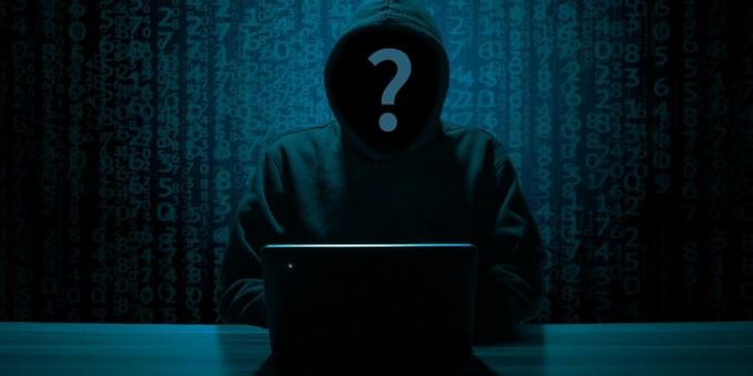 Das Gesicht eines anonymen Hackers in einem schwarzen Kapuzenpulli mit einem PC auf dem Tisch