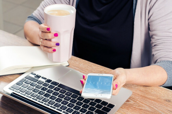 Frau, die Kaffee auf Telefon und Mac trinkt