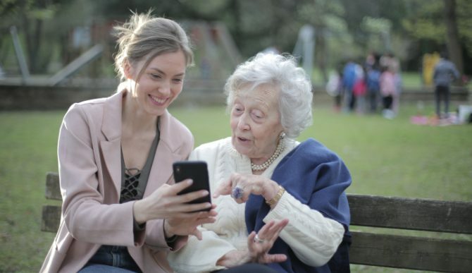 Eine junge Frau und eine alte Frau, die ein Telefon auf der Bank betrachten