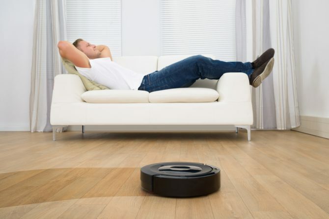 Mann, der auf Sofa mit Roboter-Staubsauger auf Hartholzboden entspannt