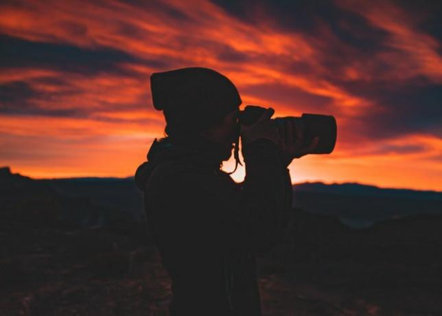 Person, die eine Kamera bei Sonnenuntergang hält