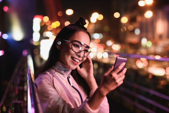 glückliches asiatisches Mädchen, das Video-Chat mit Smartphone und in Ohrkopfhörern hat