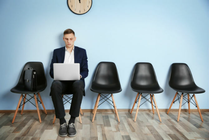 Mann, der am Laptop unter Uhr arbeitet